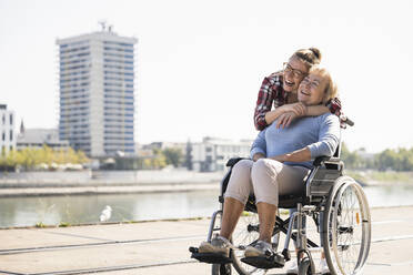 Young woman head to head with her laughing grandmother sitting in wheelchair - UUF19553