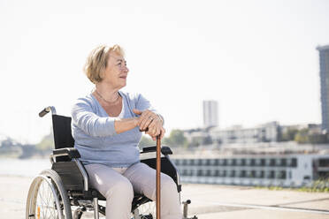 Senior woman sitting in wheelchair, with walking stick - UUF19556