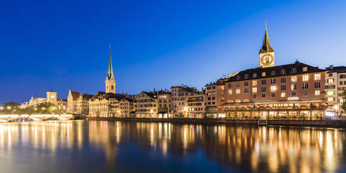 Switzerland, Canton of Zurich, Zurich, River Limmat and old town buildings along illuminated Limmatquai street at dusk - WDF05555