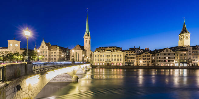 Schweiz, Kanton Zürich, Zürich, Fluss Limmat und Altstadtgebäude entlang der beleuchteten Limmatquai-Straße in der Abenddämmerung - WDF05556