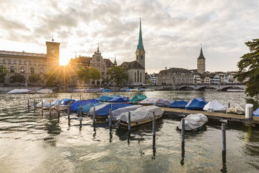 Switzerland, Canton of Zurich, Zurich, Covered boats moored on river Limmat at sunset with old town waterfront in background - WDF05559