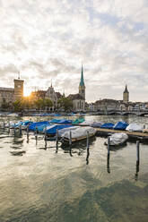 Switzerland, Canton of Zurich, Zurich, Covered boats moored on river Limmat at sunset with old town waterfront in background - WDF05560