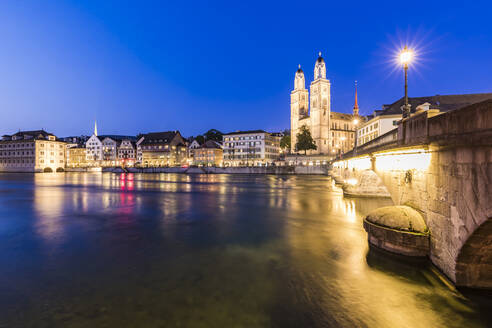 Schweiz, Kanton Zürich, Zürich, Fluss Limmat, Münsterbrücke und Altstadtgebäude entlang der beleuchteten Limmatquai-Straße in der Abenddämmerung - WDF05563