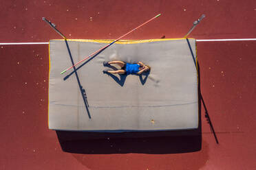 Germany, Baden-Wurttemberg, Winterbach, Female athlete lying on mat after failed high jump - STSF02338