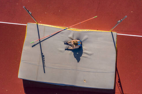 Germany, Baden-Wurttemberg, Winterbach, Female athlete sitting on mat after failed high jump - STSF02339