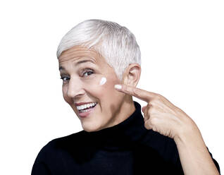 Portrait of mature woman with beauty cream on her face against white background - RAMF00094