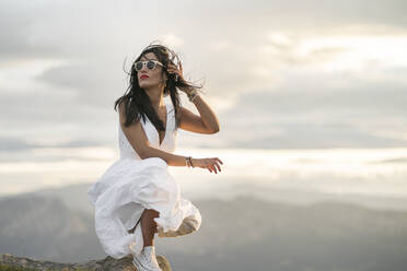 Junge Frau im weißen Kleid auf einem Aussichtspunkt bei Sonnenuntergang - MTBF00169