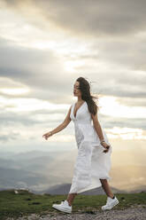 Junge Frau im weißen Kleid auf einem Aussichtspunkt bei Sonnenuntergang - MTBF00171