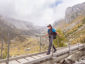 Wanderer, der über einen Steg in den Bergen geht, Naturpark Adamello, Italien - LAF02410