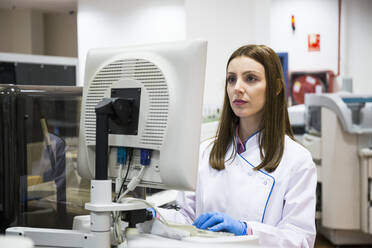 Young woman in white apparel using sample analyzer while working in research laboratory - ABZF02811