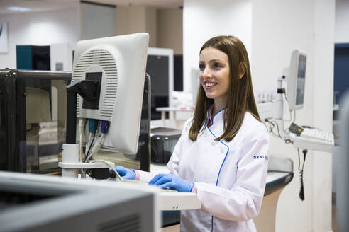 Young woman in white apparel using sample analyzer while working in research lab - ABZF02812