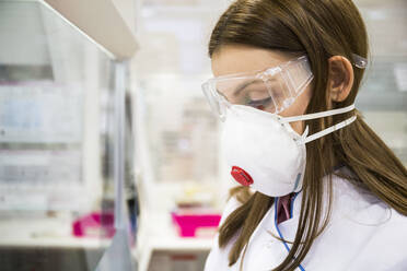 Junge Frau mit Schutzmaske und Schutzbrille bei der Arbeit in einem Labor - ABZF02816