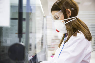 Junge Frau mit Schutzmaske und Schutzbrille bei der Arbeit in einem Labor - ABZF02817