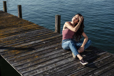 Junge Frau mit geschlossenen Augen, die auf dem Steg sitzt, Starnberger See, Deutschland - WFF00153