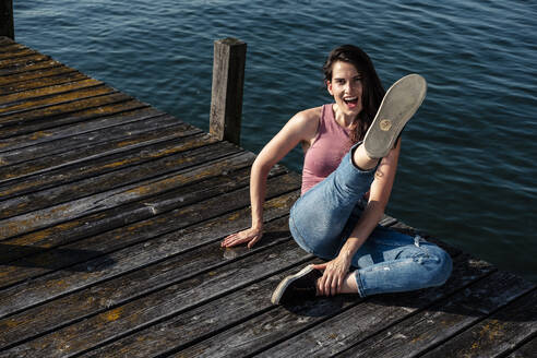 Porträt einer schreienden jungen Frau, die auf einem Steg sitzt und in die Luft tritt, Starnberger See, Deutschland - WFF00154