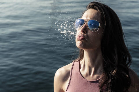 Porträt einer jungen Frau mit Sonnenbrille, die Wasser schnupft, lizenzfreies Stockfoto