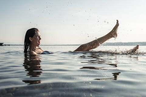 Junge Frau beim Baden im Starnberger See, Spritzen mit Wasser, Deutschland, lizenzfreies Stockfoto
