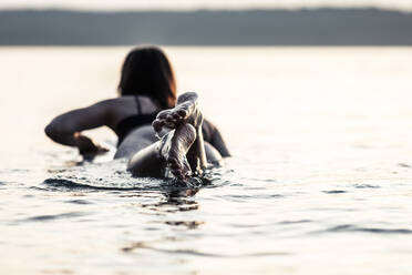 Rückenansicht einer jungen Frau auf einem Surfbrett liegend bei Sonnenuntergang, Starnberger See, Deutschland - WFF00166