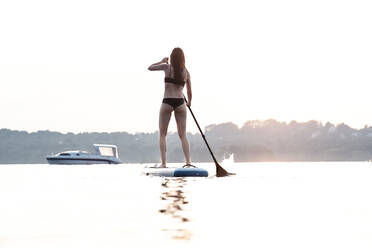 Rückenansicht einer jungen Frau, die bei Sonnenuntergang Stand-Up-Paddle-Boarding betreibt, Starnberger See, Deutschland - WFF00167