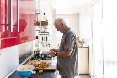 Älterer Mann bei der Zubereitung von Kartoffeln in seiner Küche - AFVF04166
