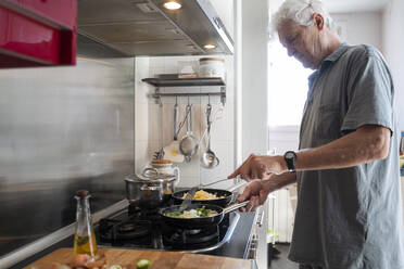 Senior man preparing food in frying pans in his kitchen - AFVF04168