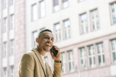 Porträt eines lachenden Geschäftsmannes am Telefon in der Stadt - AHSF01079