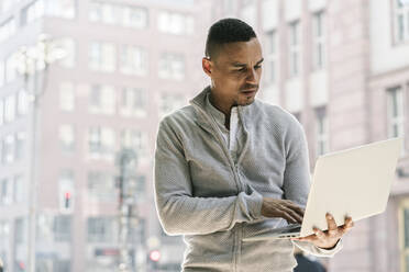 Portrait of businessman in the city using laptop - AHSF01080