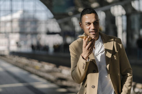 Portrait of businessman on the phone standing on platform of train station Alexanderplatz, Berlin, Germany - AHSF01098