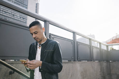 Porträt eines Mannes mit Kopfhörern und Smartphone beim Verlassen einer U-Bahn-Station - AHSF01109