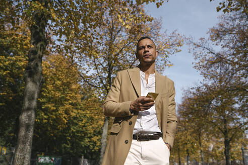 Porträt eines nachdenklichen Geschäftsmannes mit Smartphone im Herbst - AHSF01111