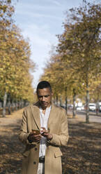 Porträt eines Geschäftsmannes mit Smartphone im Herbst - AHSF01112