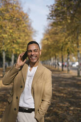 Porträt eines lachenden Geschäftsmannes am Telefon im Herbst - AHSF01114