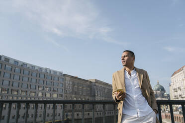 Businessman standing on a bridge with smartphone looking at distance, Berlin, Germany - AHSF01132