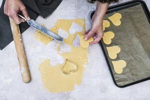 High angle close up of person using palette knife to move heart-shaped cookies onto a baking tray. - MINF12697