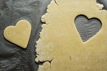 High angle close up of heart-shaped cookies cut out of cookie dough on a grey background. - MINF12699