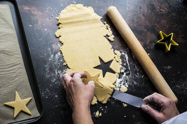 High angle close up of person lifting cut out star-shaped cookies onto a baking tray with a palette knife. - MINF12701