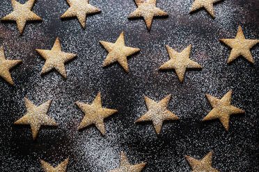 Nahaufnahme von frisch gebackenen sternförmigen Keksen, bestäubt mit Puderzucker, auf schwarzem Hintergrund. - MINF12711