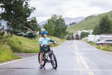 5 Jahre alter Junge, der sein Mountainbike auf einer verregneten Straße spreizt - MINF12762