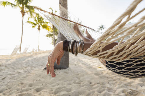 Close up of woman's arm and bracelets, relaxing resting in hammock - MINF12784