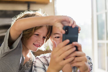 Two children, a teenager and her six year old brother holding a smart phone, taking selfies. - MINF12843