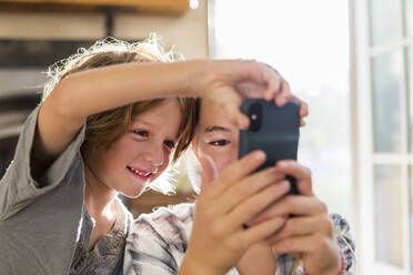 Zwei Kinder, ein Teenager und ihr sechsjähriger Bruder, halten ein Smartphone und machen Selfies. - MINF12843