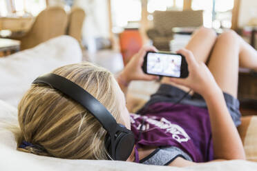 13-jähriges Mädchen zu Hause, das Kopfhörer trägt und auf sein Smartphone schaut - MINF12849