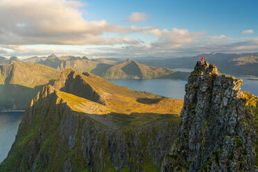 Man standing at the top of a pinnacle with a view over the landscape, Senja Island, Troms - MINF12885