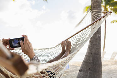 Frau in Hängematte, die ihr Smartphone benutzt - MINF12890