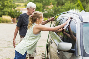 Älterer Mann, Großvater und seine 13 Jahre alte Enkeltochter waschen gemeinsam ein Auto in der Einfahrt - MINF12905