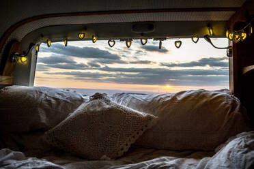 Camper van with cushion and fairy lights, view through rear window at sunset. - MINF12925