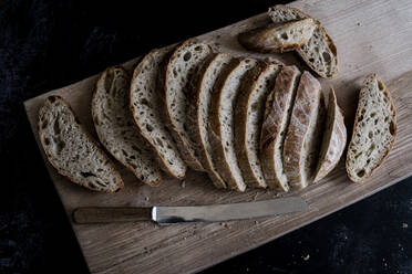 Einen Laib frisch geschnittenes Schwarzbrot auf einem Brotbrett und ein scharfes Messer - MINF12942