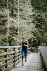 A fit young woman jogs along a bridge in a forest in Washington - CAVF68551