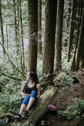 Eine Frau schreibt beim Wandern in einem Wald in Washington in ein Tagebuch - CAVF68557