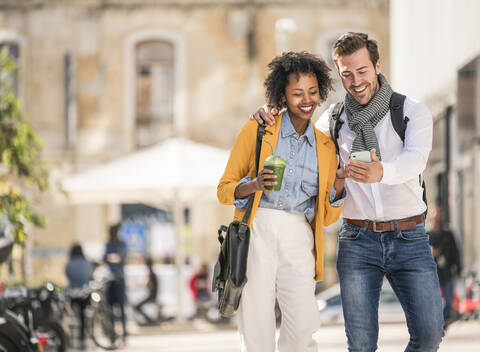 Glückliches junges Paar schaut in der Stadt auf sein Smartphone, lizenzfreies Stockfoto